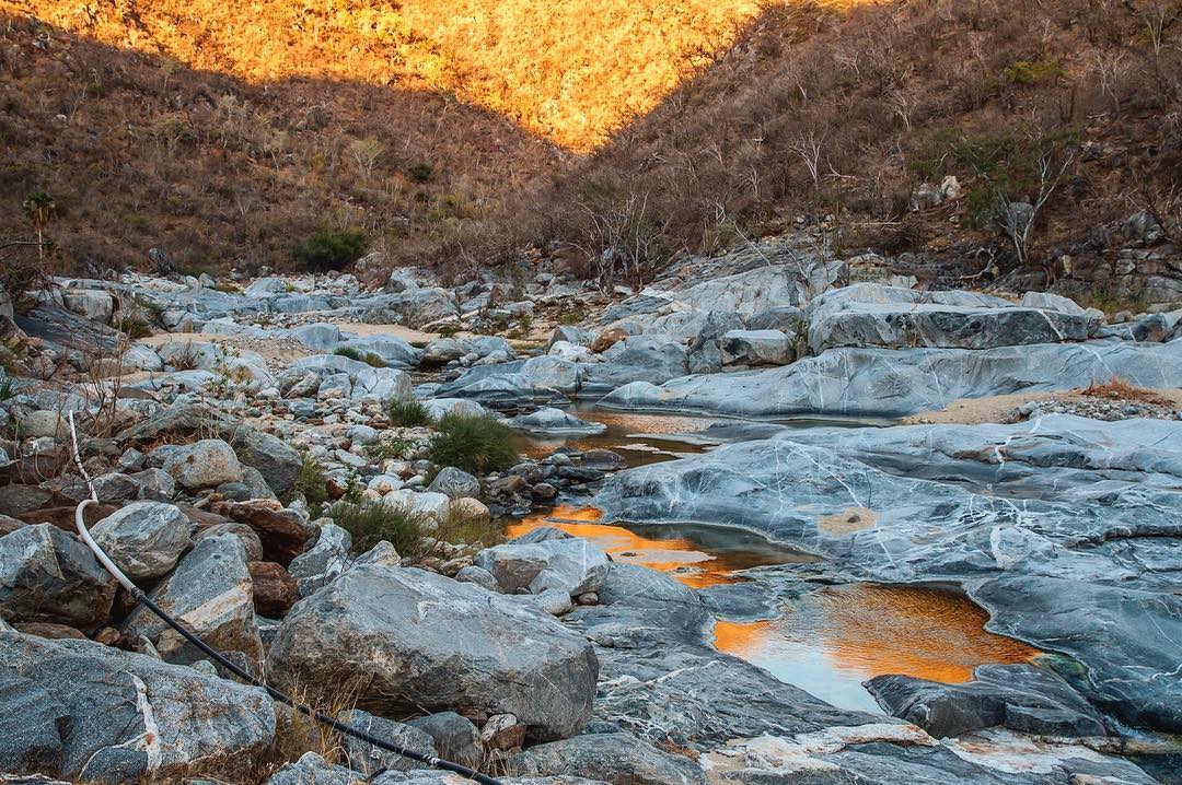 ⠀ Sunrise in Boca de la Sierra ⠀ Before I tell you a little bit about this photo, I want to invite you to follow me this coming week for some amazing pictures of one of the most exotic places on Earth: Tierra del Fuego! Tomorrow I begin the long journey down to Ushuaia where, on May 23, I will join @adventure.travel_, @patagoniacl, @turismotdf and an awesome group of people from the adventure travel industry to discover some of the most amazing adventures this region can offer. ⠀ And so! I recently went camping back to Boca de la Sierra, and this time me and my camera were up in time for one of the most magical moments you can experience in this spot: sunrise. ⠀ It starts as the Sun begins to rise and soft light starts flooding into the canyon, but the real magic happens when its direct light starts creeping in it. The surrounding hills get covered in a veil of bright orange glow and bounce beautiful warm light onto the landscape still in shade. ⠀ Once there’s enough orange on the hills, it’s easy to find their reflection on the small bodies of water you can find all over, which creates a lava-like effect on them. ⠀ With all the beautiful moments, memories and sights this place has given me, it’s still and will always be one of my favorite get-away places close to home. ⠀ Oh! and in case you’re wondering what that big hose on the left is, that’s how local farmers pull water down from small dams they built higher into the canyon to water their crops. You can see it again in a previous picture of this place that I uploaded here, and you can even see the discreet dam in the background. Can you find it?